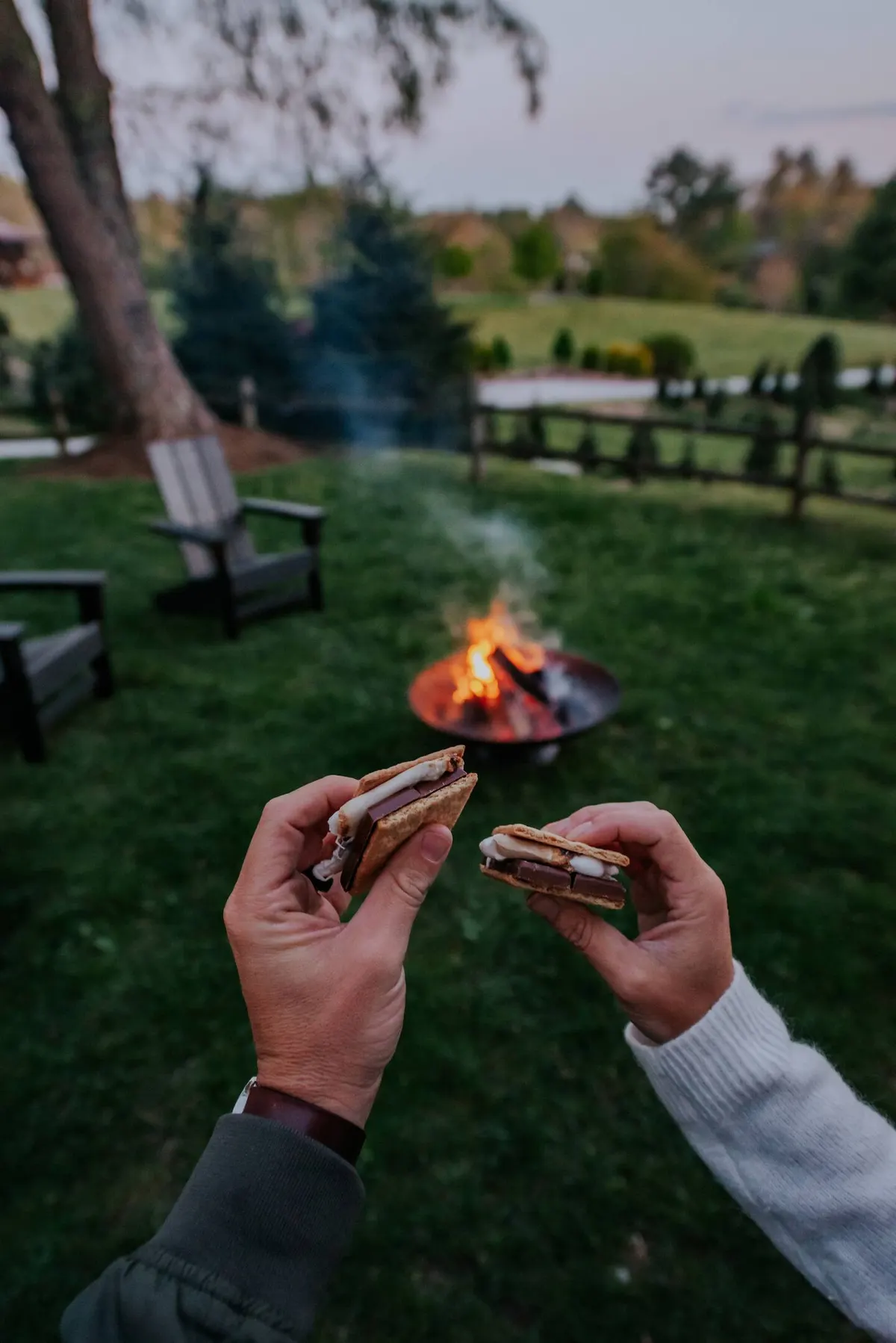 Two hands holding s'mores by the fire pit